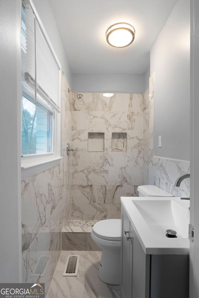 bathroom featuring vanity, a tile shower, tile walls, and toilet