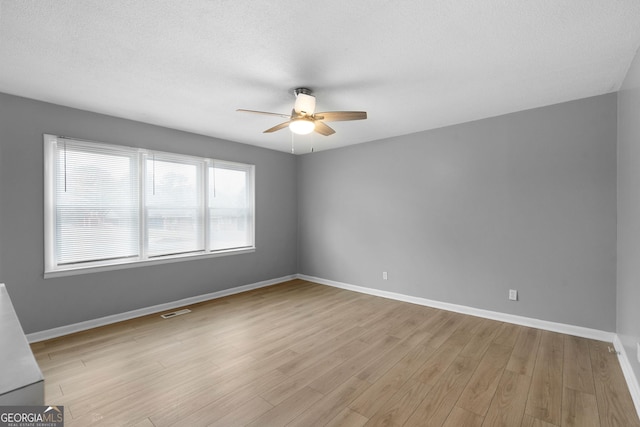 empty room with ceiling fan, a textured ceiling, and light wood-type flooring