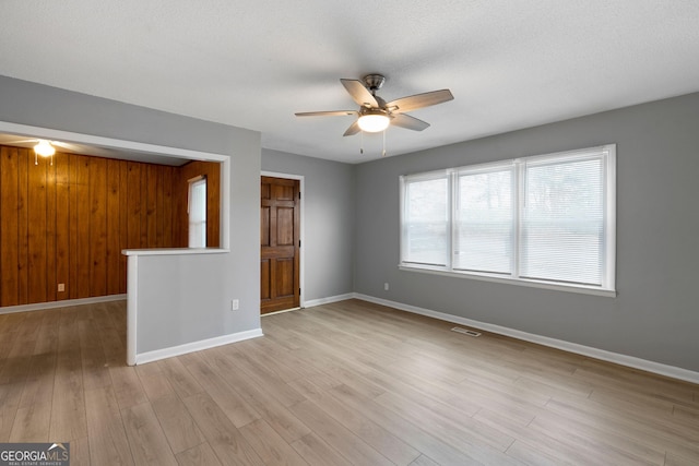 unfurnished living room with light hardwood / wood-style flooring, ceiling fan, and wood walls