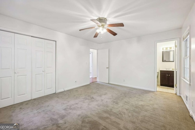 unfurnished bedroom featuring ceiling fan, light colored carpet, ensuite bath, and a closet