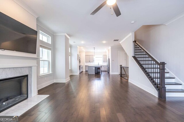 unfurnished living room with crown molding, ceiling fan, a high end fireplace, and dark wood-type flooring