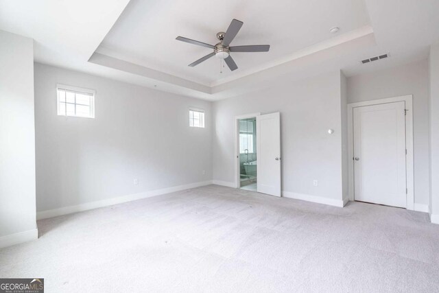 carpeted empty room with a tray ceiling, plenty of natural light, and ceiling fan