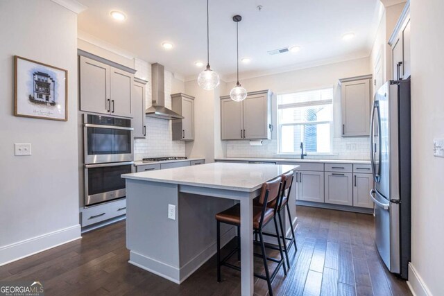 kitchen with wall chimney exhaust hood, a center island, dark hardwood / wood-style flooring, pendant lighting, and stainless steel appliances