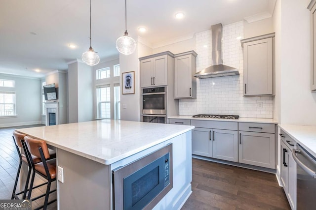 kitchen with ornamental molding, wall chimney exhaust hood, appliances with stainless steel finishes, and light stone countertops