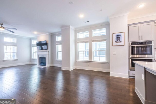 unfurnished living room featuring crown molding, ceiling fan, plenty of natural light, and dark hardwood / wood-style floors