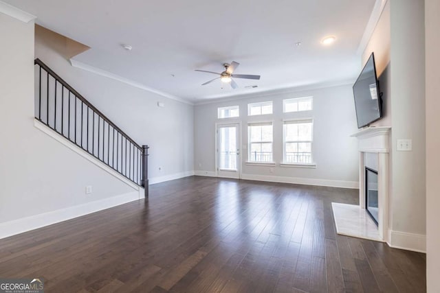 unfurnished living room with a ceiling fan, baseboards, stairway, dark wood finished floors, and crown molding