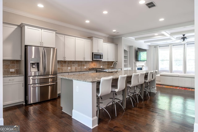 kitchen with dark wood-type flooring, a breakfast bar area, appliances with stainless steel finishes, a kitchen island with sink, and light stone counters