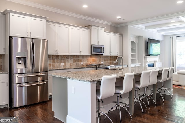 kitchen featuring light stone counters, stainless steel appliances, a breakfast bar area, and a center island with sink