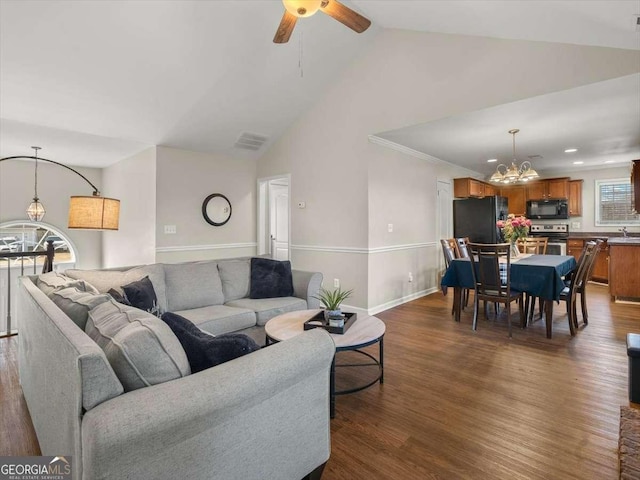 living room featuring ceiling fan with notable chandelier, dark hardwood / wood-style flooring, and vaulted ceiling