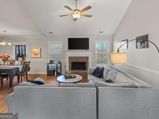 living room with high vaulted ceiling, wood-type flooring, a fireplace, and ceiling fan with notable chandelier