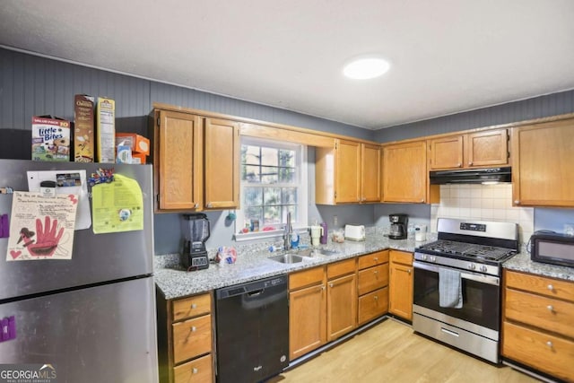 kitchen with tasteful backsplash, sink, light stone counters, black appliances, and light wood-type flooring