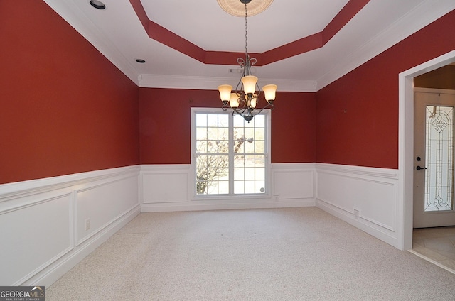 spare room featuring a raised ceiling, light carpet, and a chandelier