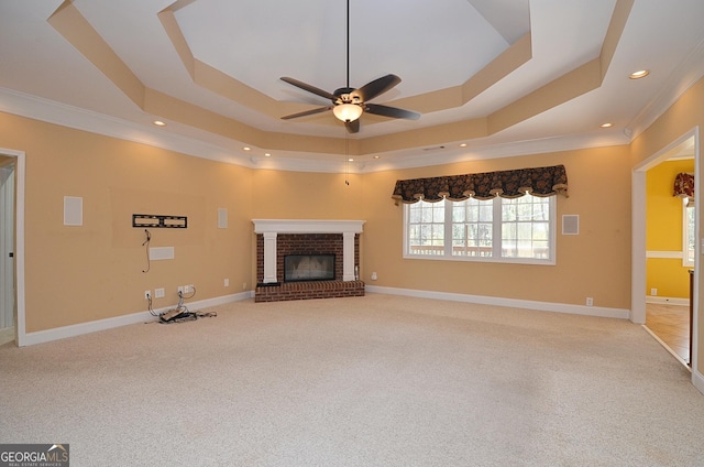 unfurnished living room featuring ceiling fan, a tray ceiling, crown molding, a brick fireplace, and light carpet