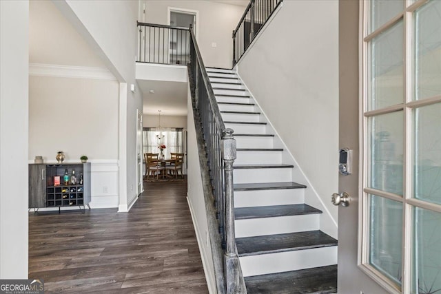 stairway with a towering ceiling, wood-type flooring, and ornamental molding