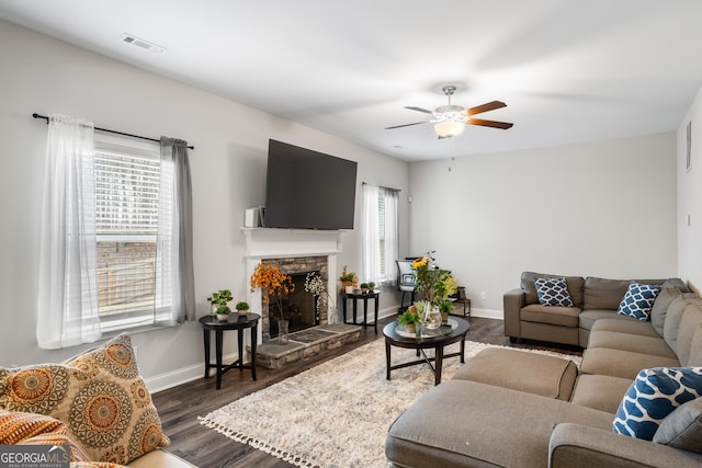 living room featuring a stone fireplace, dark hardwood / wood-style floors, and ceiling fan