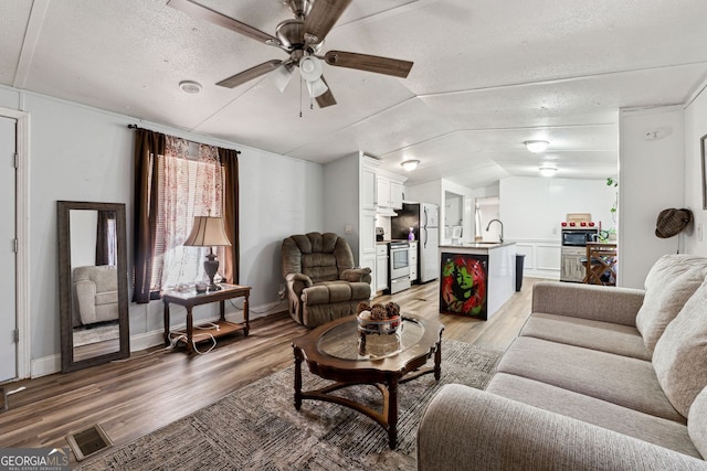 living room with sink, vaulted ceiling, a textured ceiling, ceiling fan, and hardwood / wood-style floors