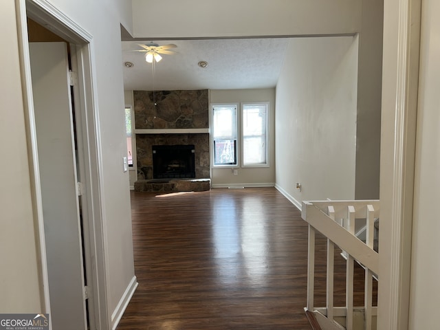 unfurnished living room featuring ceiling fan, dark wood-type flooring, a textured ceiling, and a fireplace