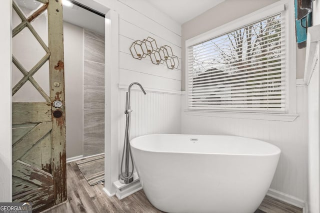 bathroom featuring wood walls, hardwood / wood-style floors, and a washtub