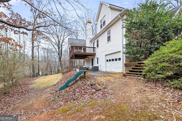 rear view of house with a wooden deck, a garage, a playground, and central air condition unit