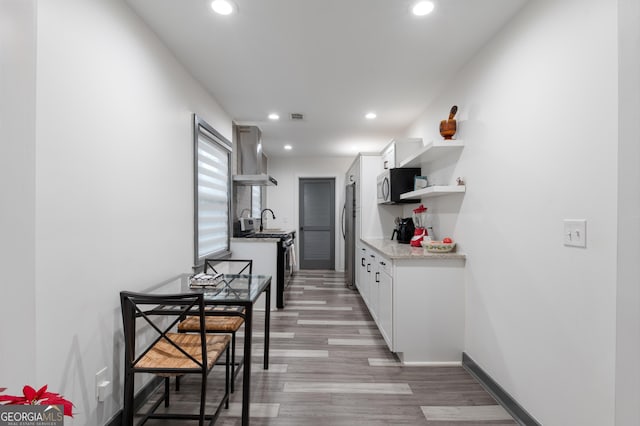 kitchen featuring sink, appliances with stainless steel finishes, white cabinets, light hardwood / wood-style floors, and wall chimney range hood