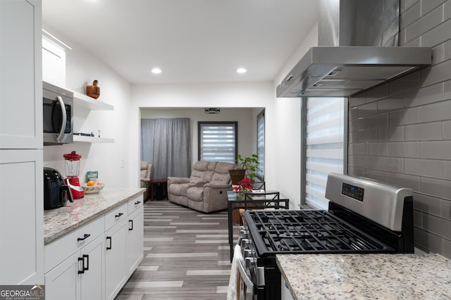 kitchen featuring white cabinetry, range hood, stainless steel appliances, light stone counters, and light wood-type flooring