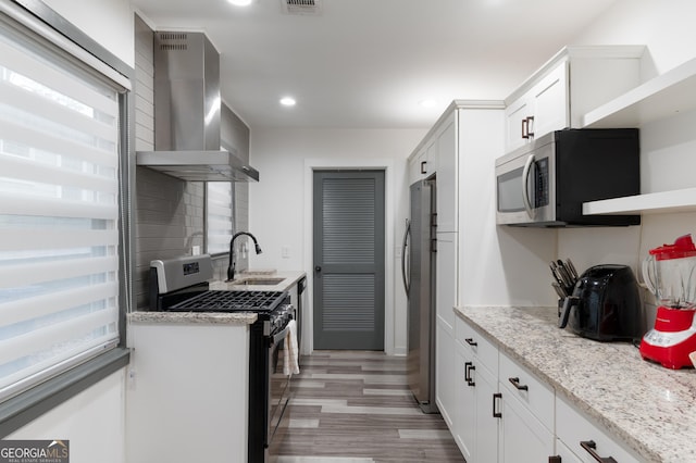 kitchen featuring appliances with stainless steel finishes, sink, white cabinets, light stone countertops, and wall chimney exhaust hood