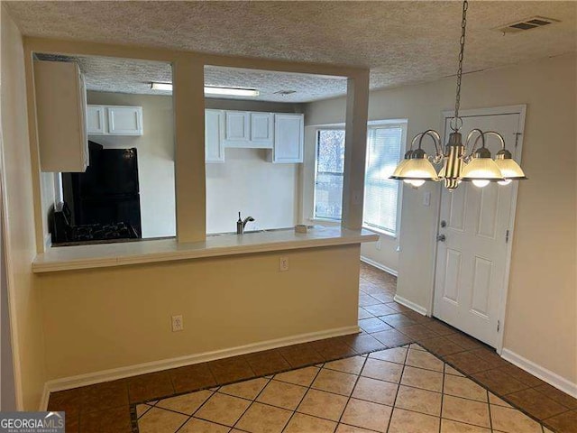 kitchen featuring light tile patterned flooring, decorative light fixtures, white cabinetry, black fridge, and a textured ceiling