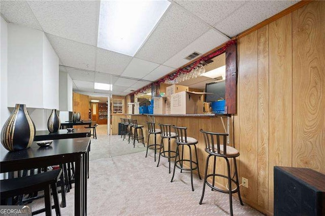 dining space with indoor bar, a paneled ceiling, and wood walls