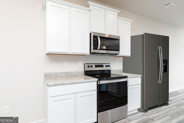 kitchen with appliances with stainless steel finishes, light stone countertops, light hardwood / wood-style floors, and white cabinets