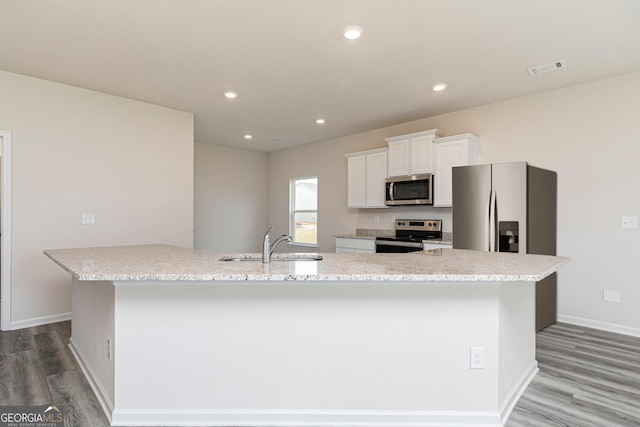 kitchen with sink, appliances with stainless steel finishes, wood-type flooring, white cabinets, and a large island with sink