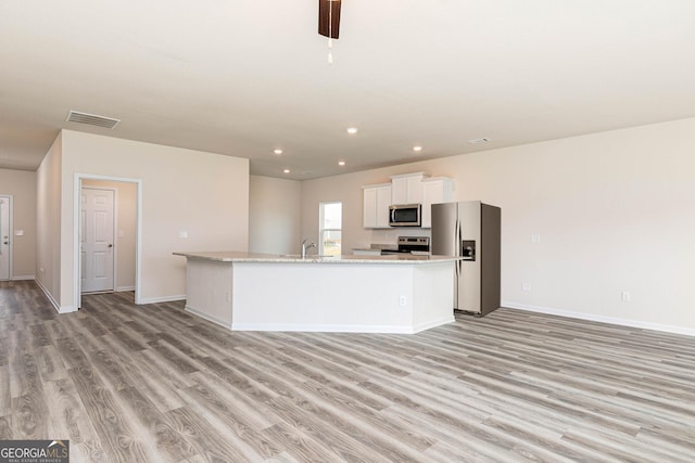 kitchen featuring white cabinetry, appliances with stainless steel finishes, a center island with sink, and light hardwood / wood-style flooring