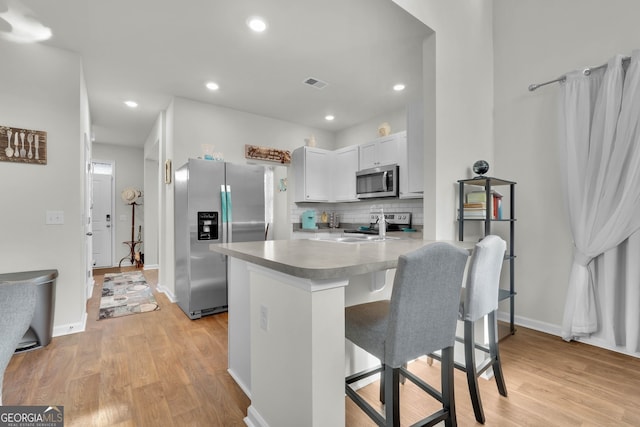 kitchen featuring white cabinets, a kitchen bar, kitchen peninsula, stainless steel appliances, and light hardwood / wood-style flooring