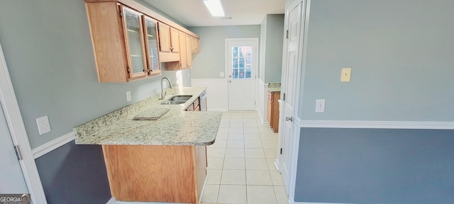 kitchen with light tile patterned flooring, sink, stainless steel dishwasher, kitchen peninsula, and light stone countertops