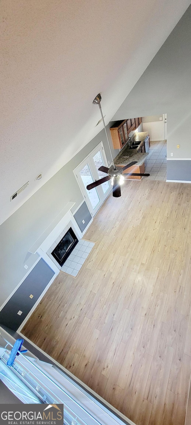 unfurnished living room with ceiling fan, lofted ceiling, light hardwood / wood-style flooring, and a textured ceiling