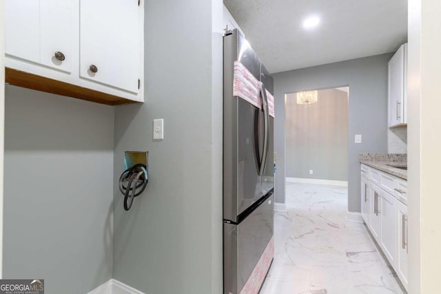 kitchen featuring white cabinetry, light stone counters, stainless steel refrigerator, and an inviting chandelier