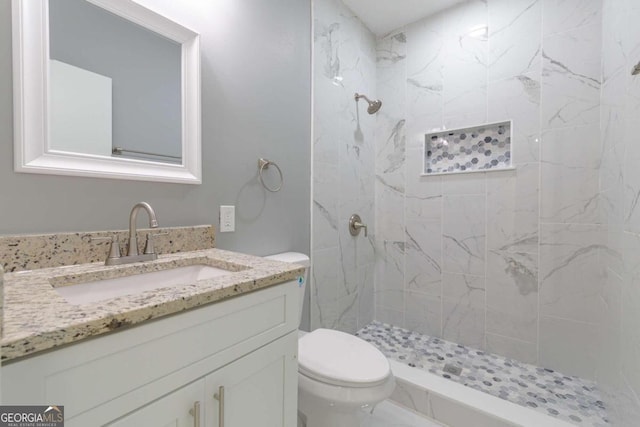 bathroom featuring vanity, a tile shower, and toilet