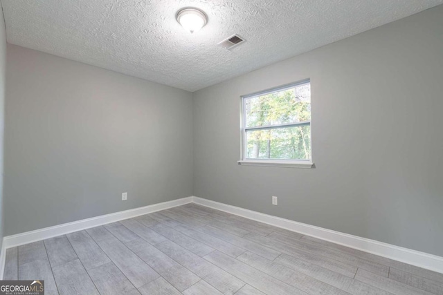 spare room with a textured ceiling and light hardwood / wood-style floors