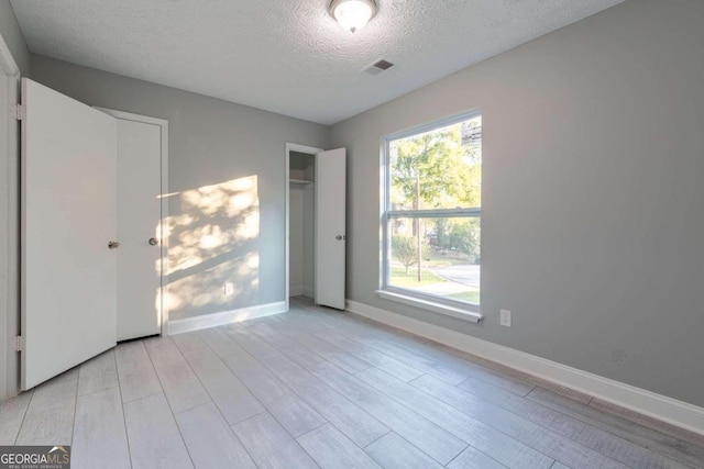 unfurnished room with a textured ceiling and light wood-type flooring