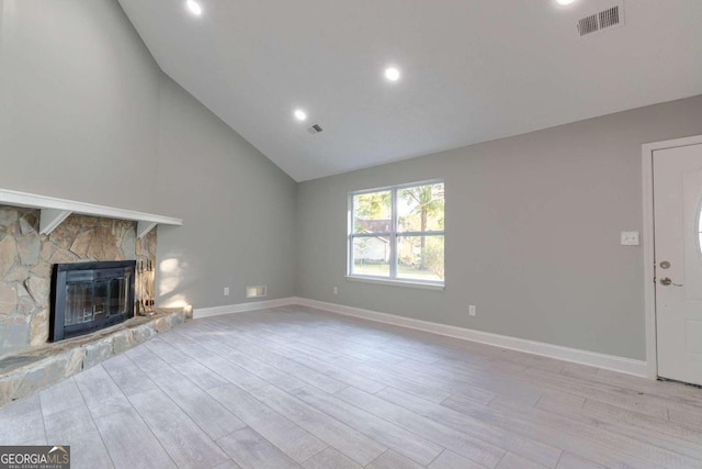 unfurnished living room featuring a stone fireplace, high vaulted ceiling, and light wood-type flooring