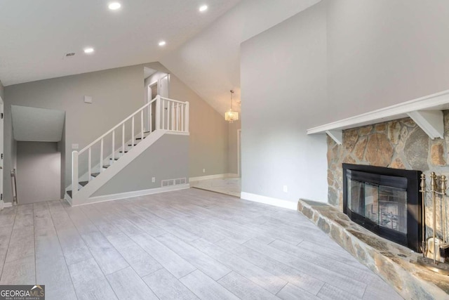 unfurnished living room with vaulted ceiling, a stone fireplace, and light hardwood / wood-style floors