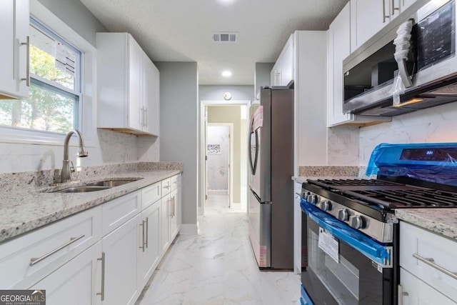 kitchen with light stone counters, stainless steel appliances, sink, and white cabinets