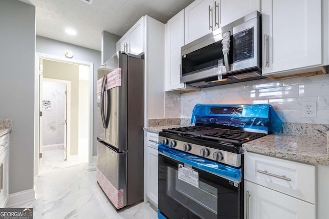 kitchen featuring white cabinets, decorative backsplash, stainless steel appliances, light stone countertops, and a textured ceiling