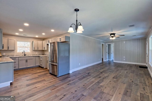 kitchen with dark wood-type flooring, stainless steel refrigerator, pendant lighting, light stone countertops, and white cabinets