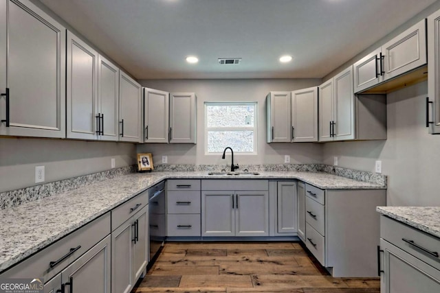 kitchen with dishwasher, wood-type flooring, sink, gray cabinetry, and light stone countertops