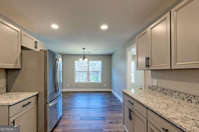 kitchen with stainless steel refrigerator, decorative light fixtures, a chandelier, light stone counters, and dark wood-type flooring