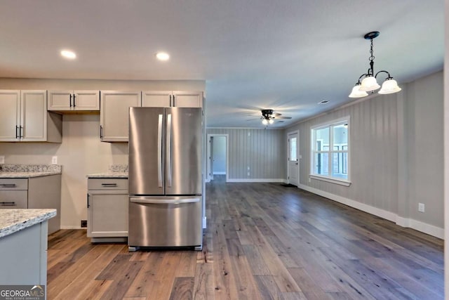 kitchen featuring stainless steel refrigerator, ceiling fan, hanging light fixtures, light stone counters, and dark hardwood / wood-style flooring