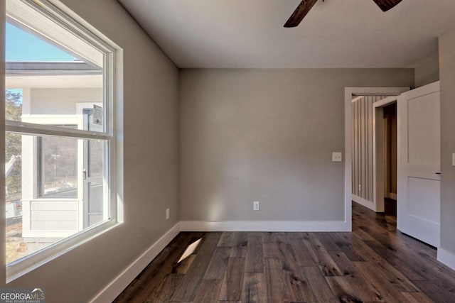 empty room with dark hardwood / wood-style flooring, a wealth of natural light, and ceiling fan