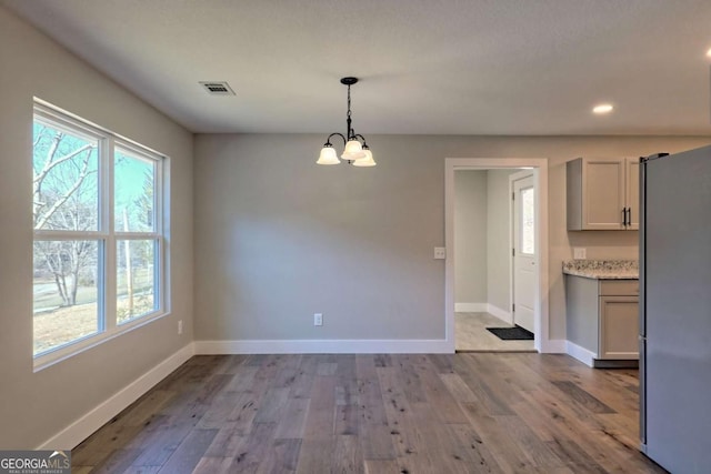 unfurnished dining area with an inviting chandelier and light wood-type flooring