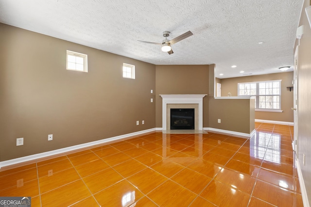 unfurnished living room with ceiling fan, tile patterned floors, and a textured ceiling