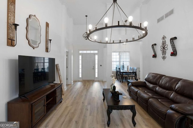 living room featuring a notable chandelier, a towering ceiling, and light wood-type flooring